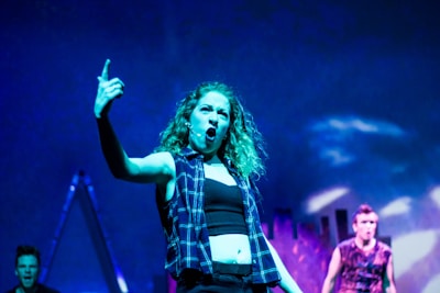 A queer comedian delivering a punchline with expressive gestures on stage.