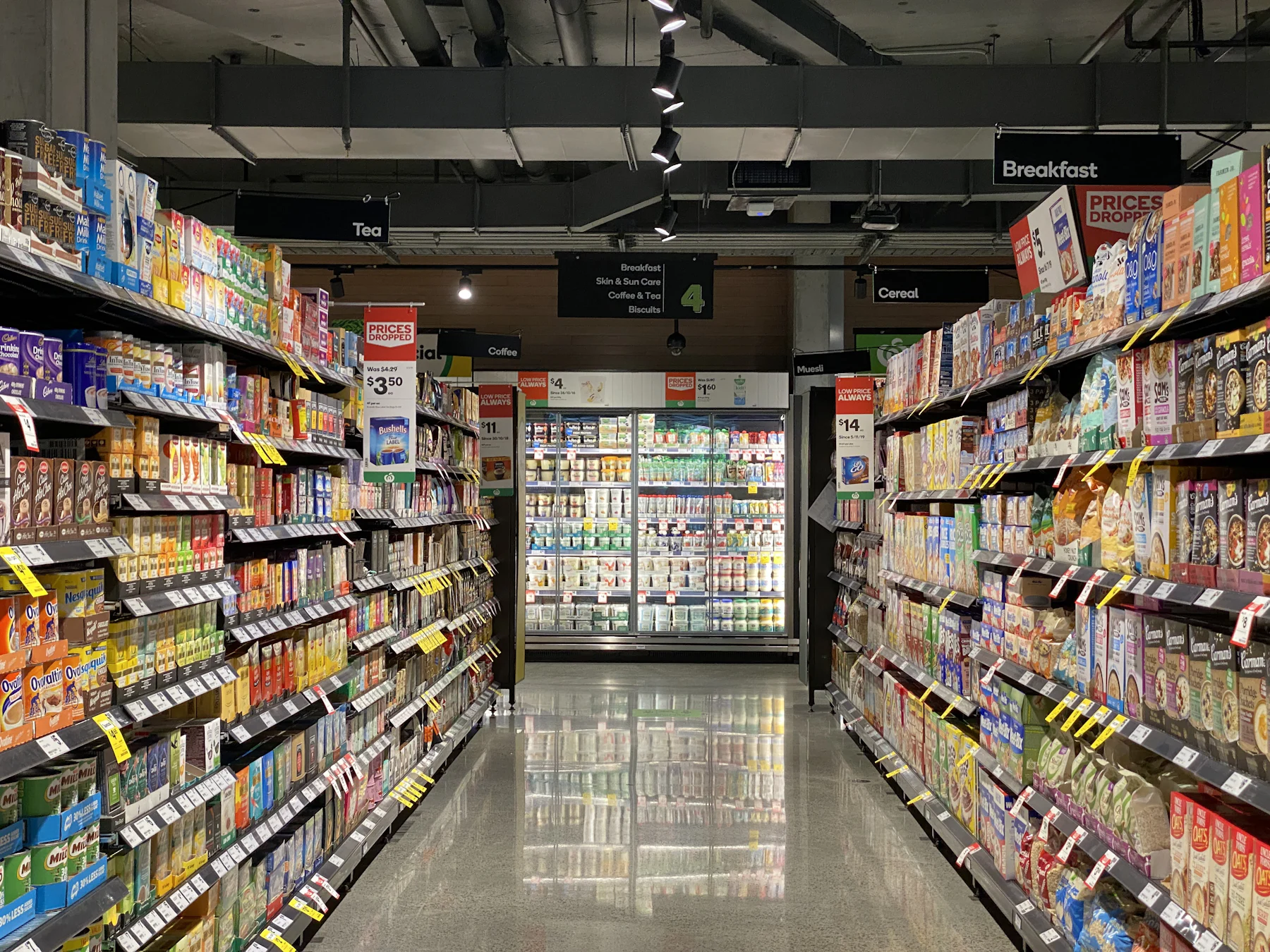 A long, softly lit grocery aisle with stocked shelves stretching toward the back of an empty store floor.