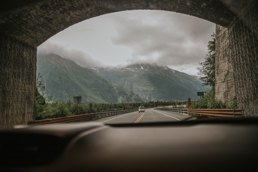 gray concrete road near green trees and mountain during daytime