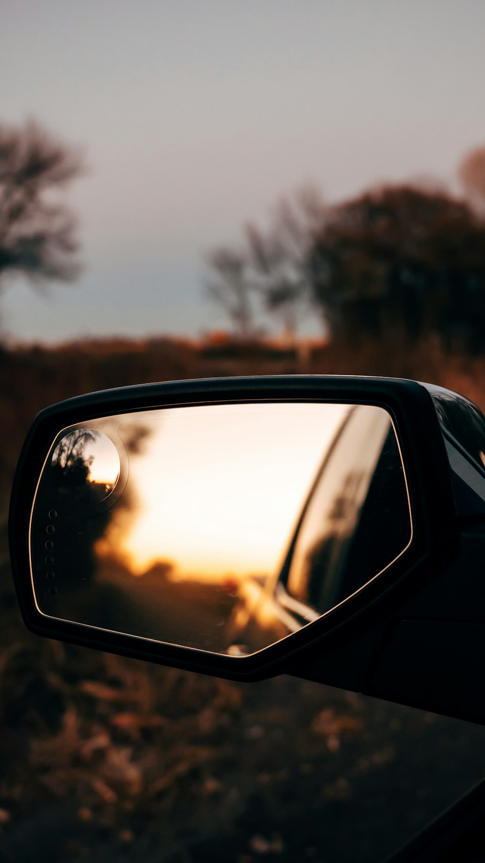 Espejo lateral del automóvil con reflejo de árboles en la carretera durante el día