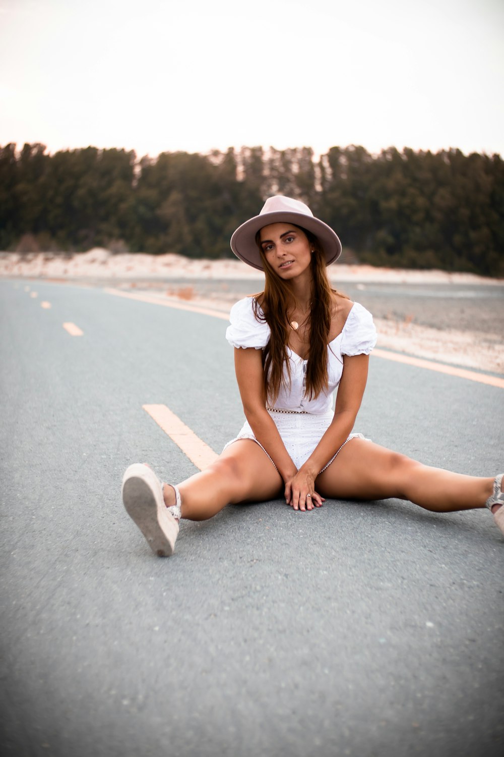 woman in white dress and brown hat sitting on gray asphalt road during daytime
