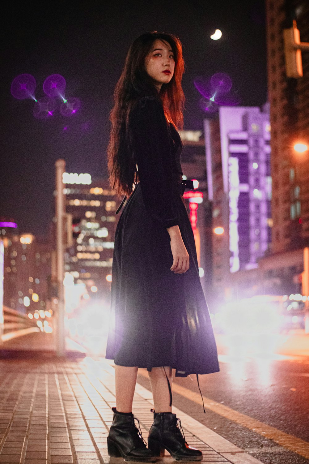 woman in black long sleeve dress standing on sidewalk during night time