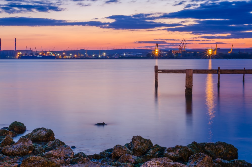 Muelle de madera marrón en el cuerpo de agua durante la puesta del sol