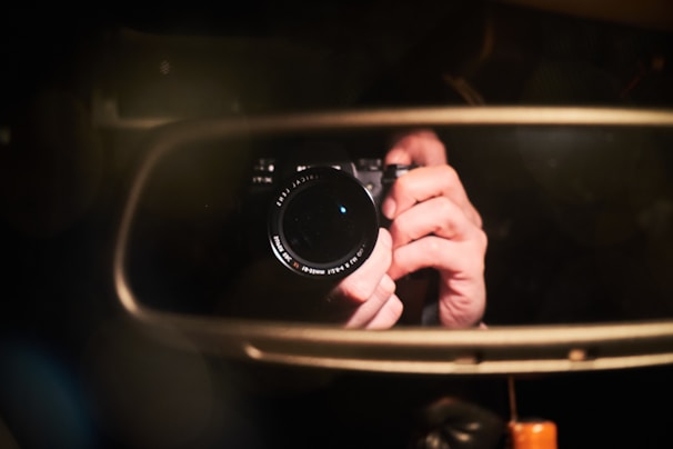 Close-up of a detective’s hand holding a camera with a zoom lens, capturing images through a car window.