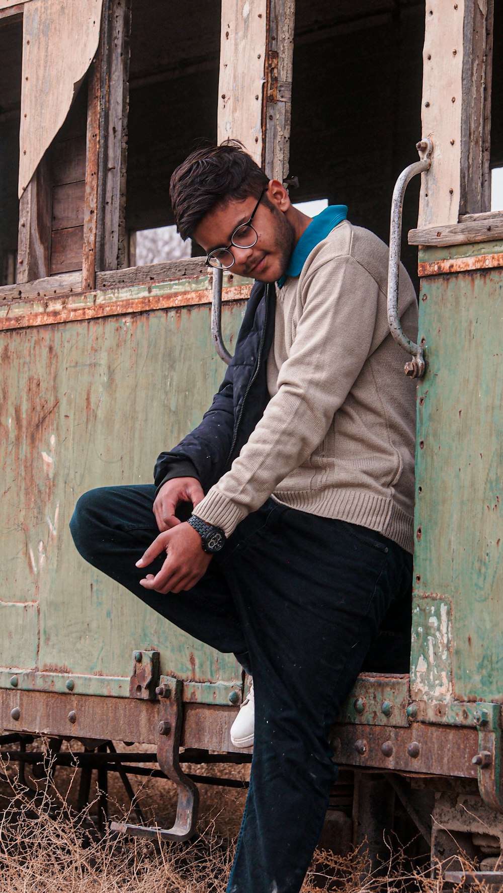 man in gray sweater and black pants sitting on green wooden door