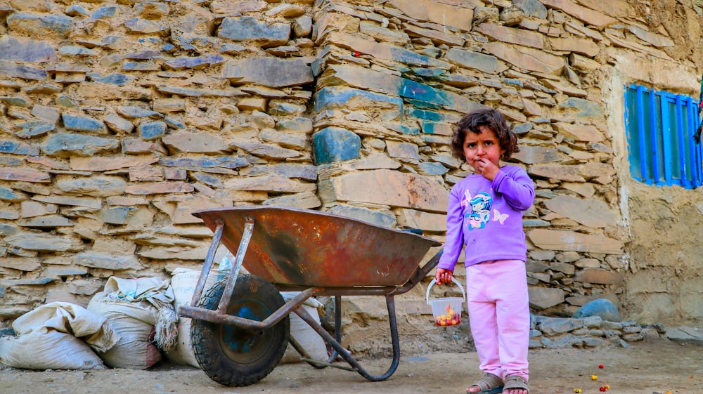 a little girl standing next to a wheelbarrow