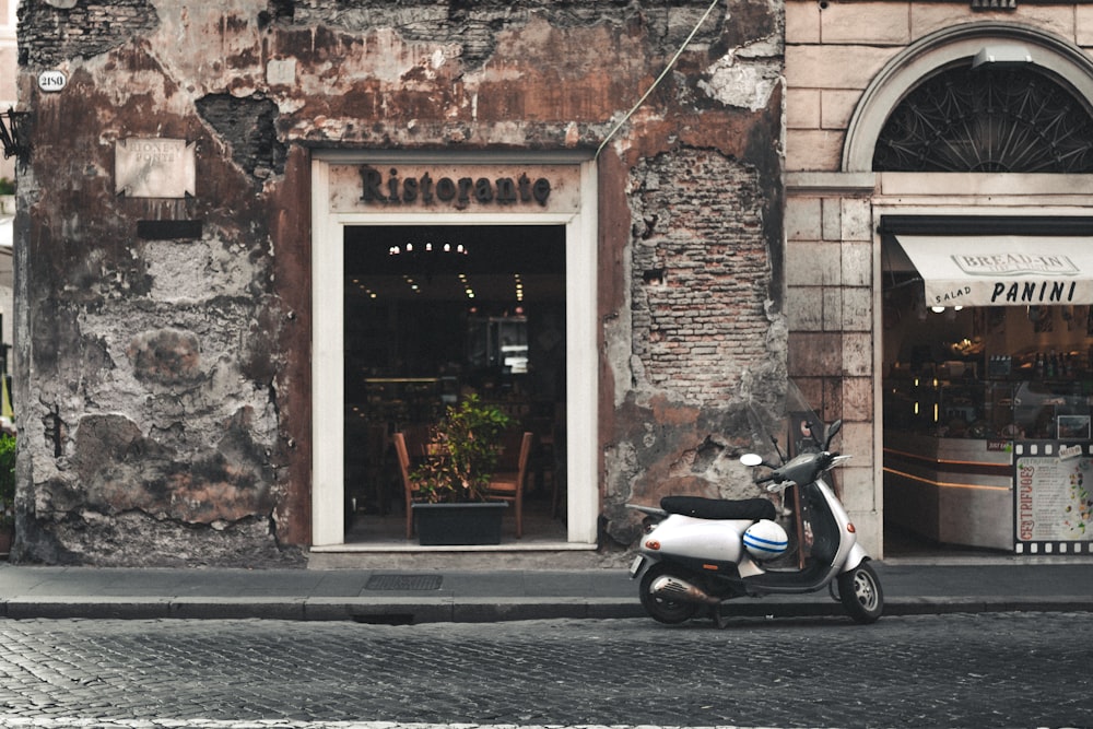 scooter blanco y negro estacionado junto a un edificio de concreto marrón durante el día