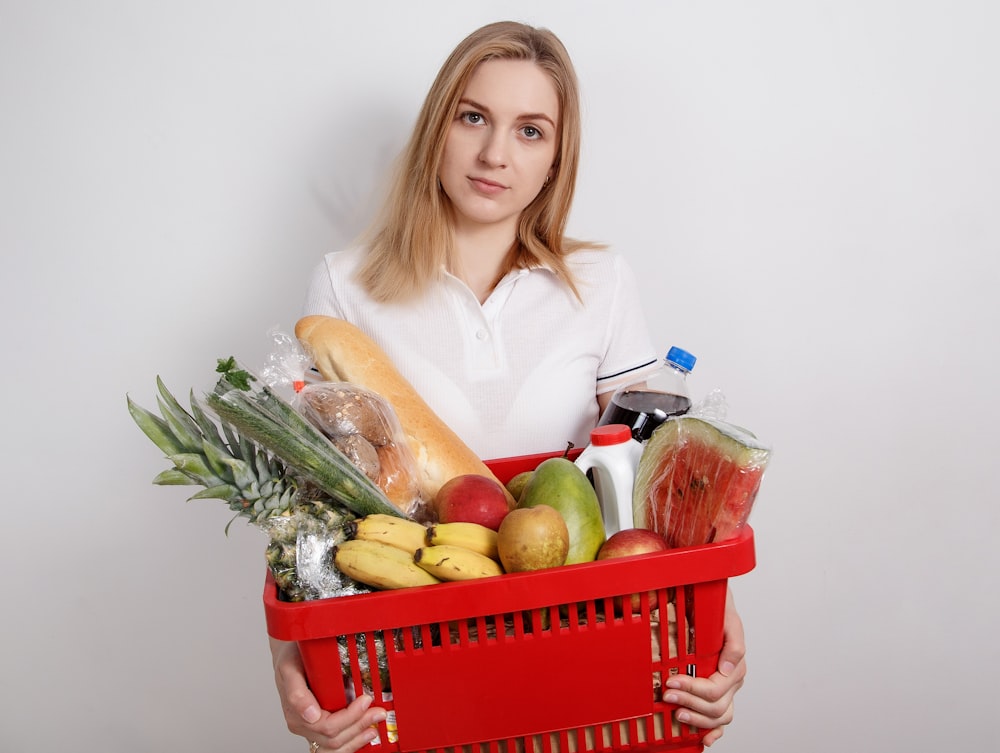 woman in white long sleeve shirt holding red plastic basket with fruits