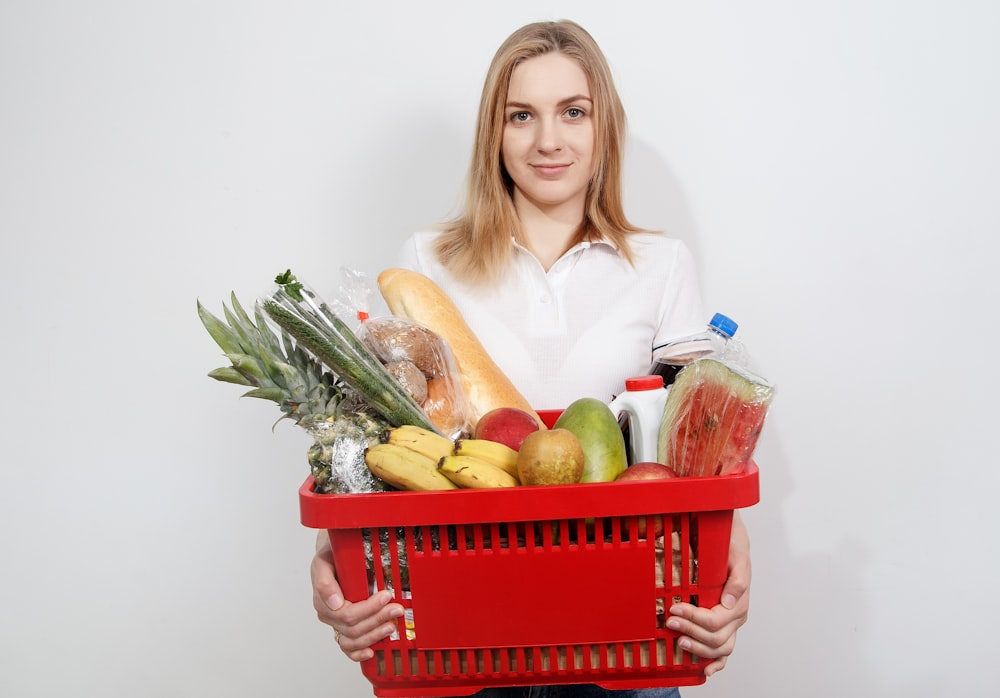 woman in white dress shirt holding red plastic basket with fruits