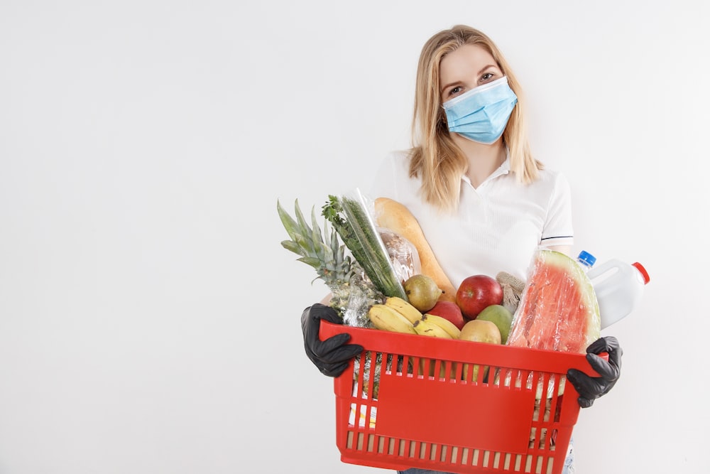 白い長袖シャツを着た女性が果物の入った赤いプラスチックのバスケットを持っている