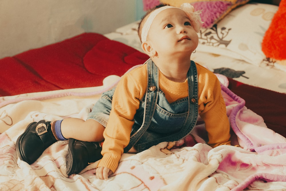 baby in orange and white jacket and black pants sitting on bed