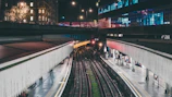 Nighttime view of a railway station entrance illuminated by bright outdoor LED advertisements.