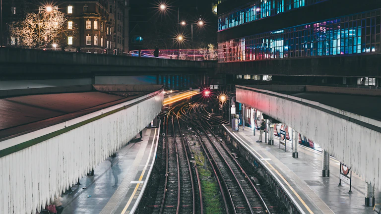 Nighttime view of a railway station entrance illuminated by bright outdoor LED advertisements.