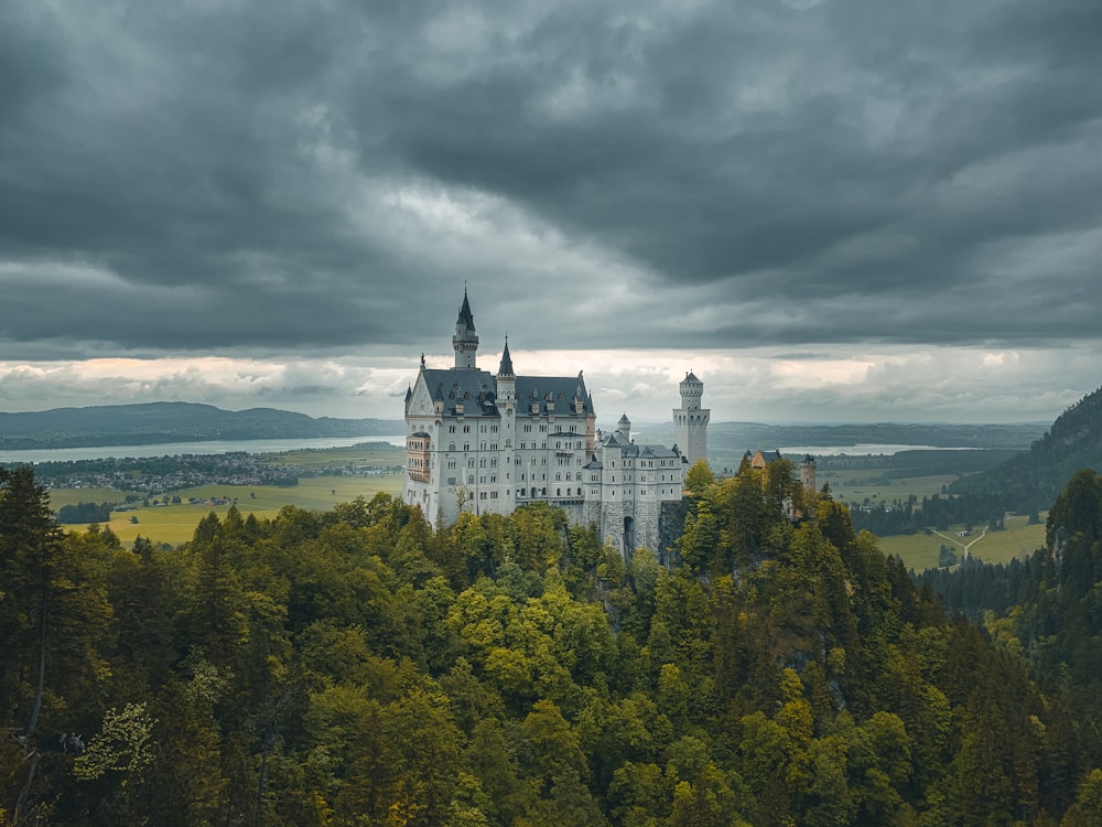 white and black castle on top of green trees under cloudy sky during daytime