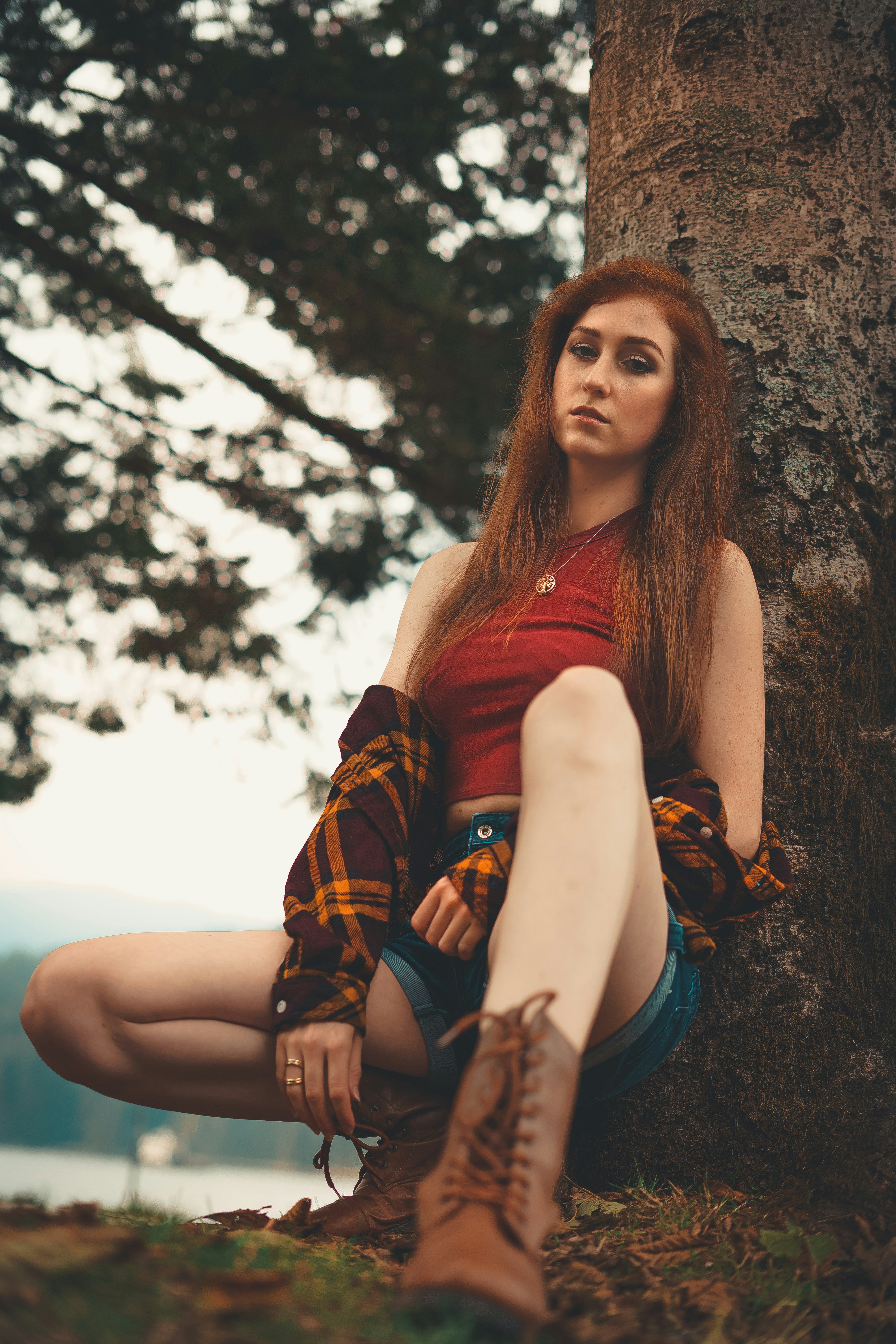 woman in red tank top and blue denim shorts sitting on brown tree branch during daytime
