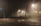 A foggy street scene with weathered church silhouette and glowing lanterns faintly visible through the mist.