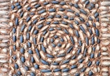 An intricate spiral pattern composed of oval-shaped stones, alternating in hues of dark blue and light beige, with a surrounding border of smaller stones. The design is interspersed with dried brown leaves, adding texture and contrast to the natural arrangement.