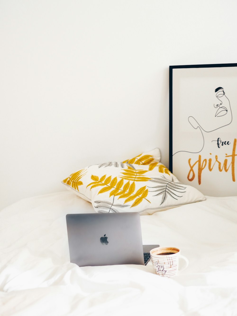 silver macbook beside white and yellow floral throw pillow