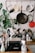 A kitchen setting features a dish rack filled with various clean kitchen utensils, including pots, pans, and glassware. Above the sink, a wooden rack holds hanging metal pots and pans. There are kitchen cleaning supplies on the counter, such as a dish soap dispenser. A green potted plant with large leaves adds a touch of nature to the scene.