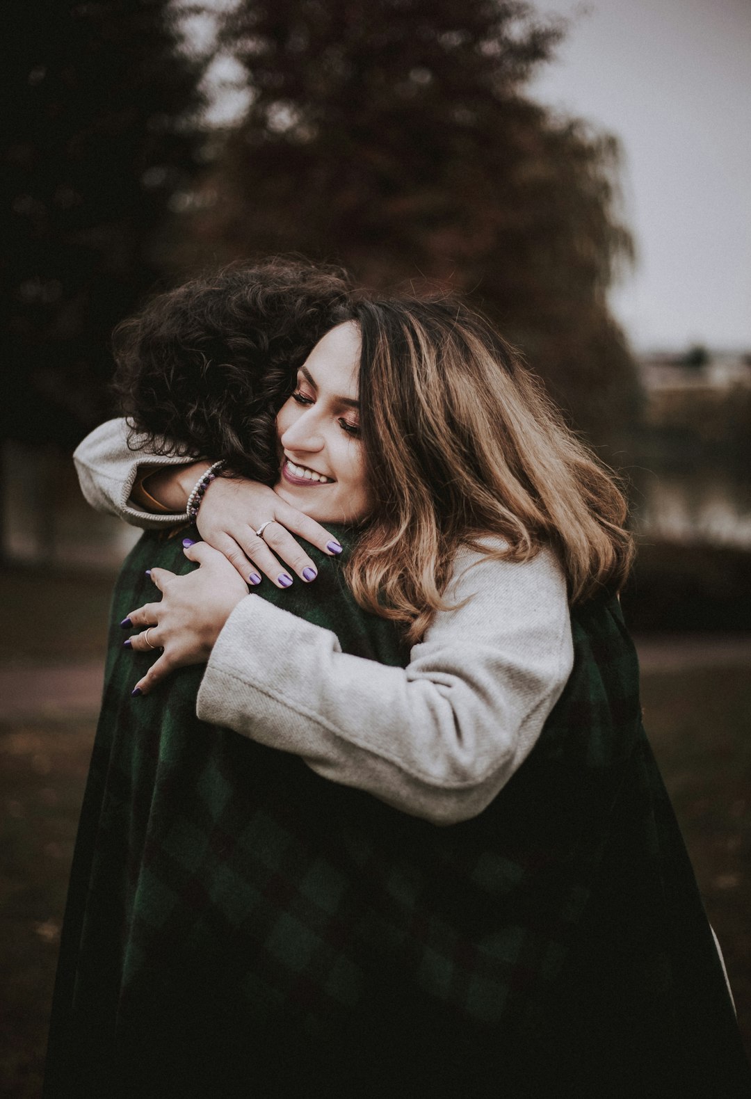 woman in gray sweater hugging man in green and black plaid dress shirt