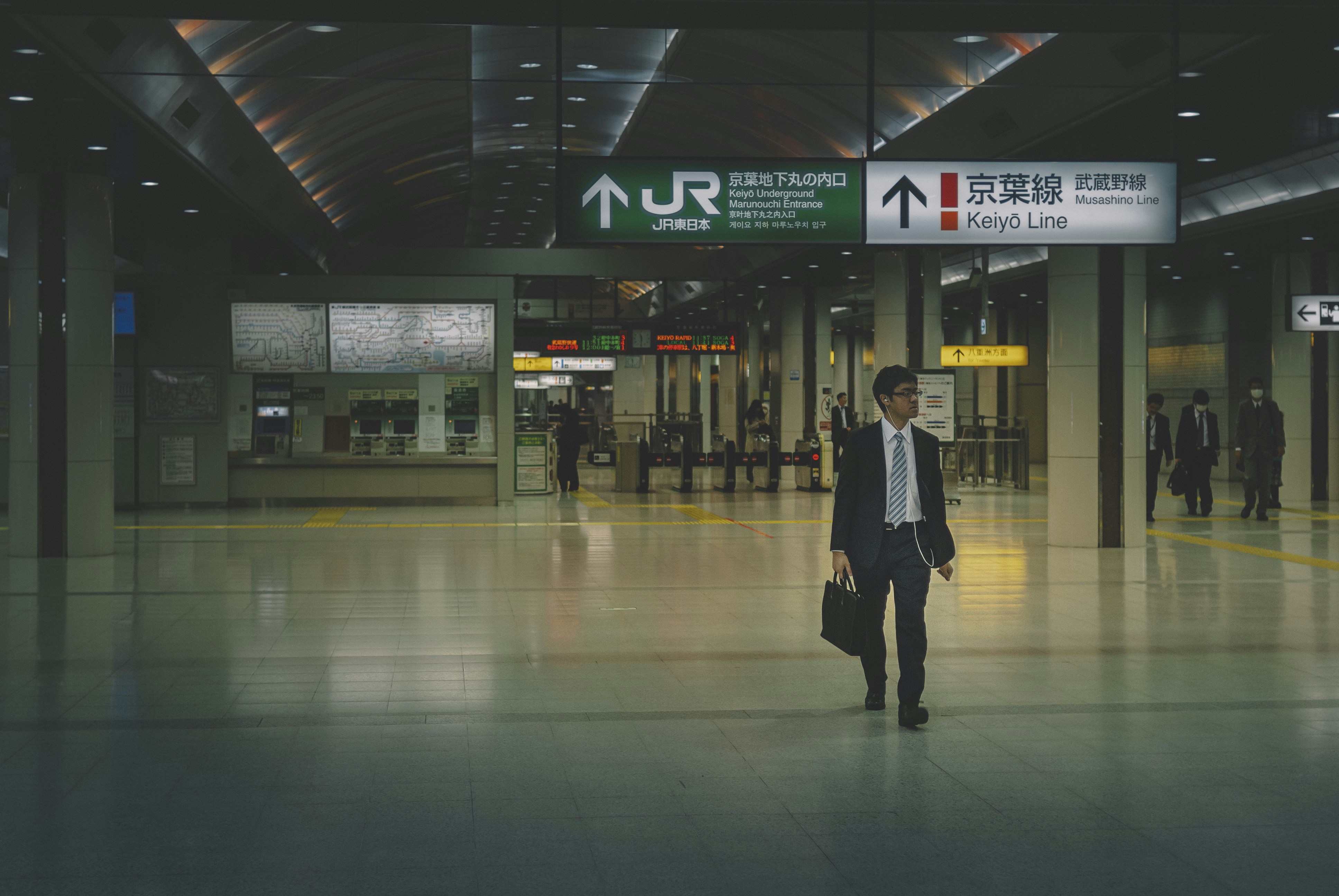 man in black jacket walking on white floor tiles, Tokyo subway.
