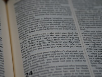 A close-up view of an open book with text, featuring dense paragraphs in a serif font. Text is clearly visible and appears to be a passage from a religious or legal context.
