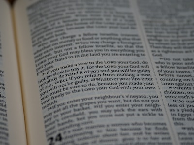 A close-up view of an open book with text, featuring dense paragraphs in a serif font. Text is clearly visible and appears to be a passage from a religious or legal context.
