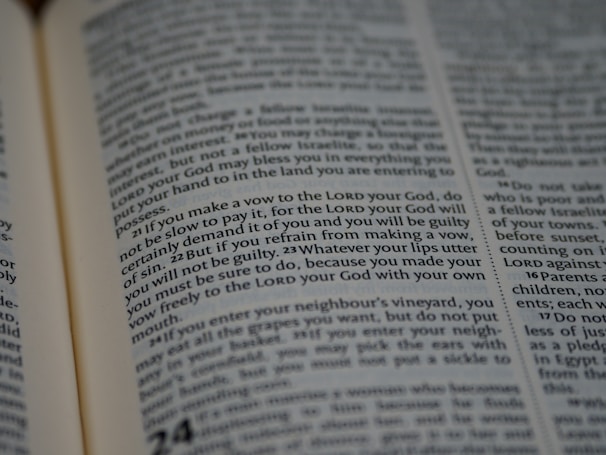 A close-up view of an open book with text, featuring dense paragraphs in a serif font. Text is clearly visible and appears to be a passage from a religious or legal context.