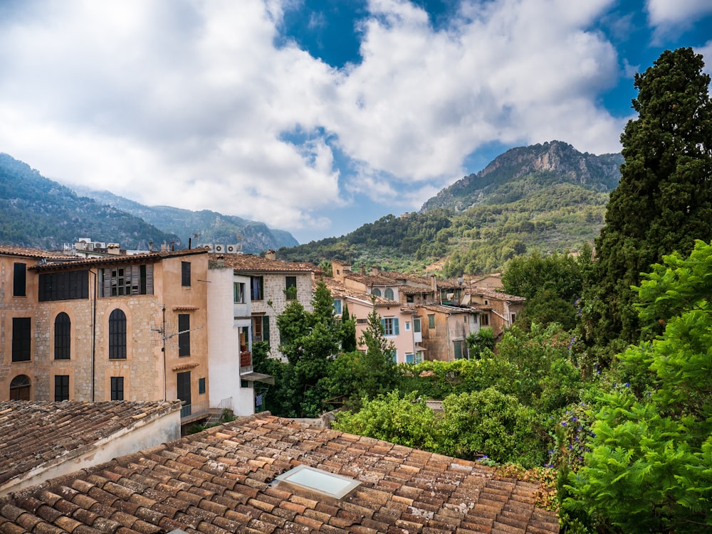 brown concrete building near green trees and mountain under white clouds and blue sky during daytime