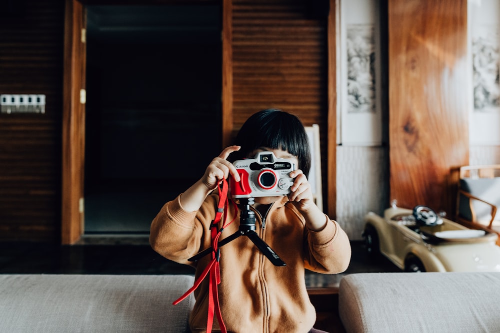 woman in brown coat holding white and red camera