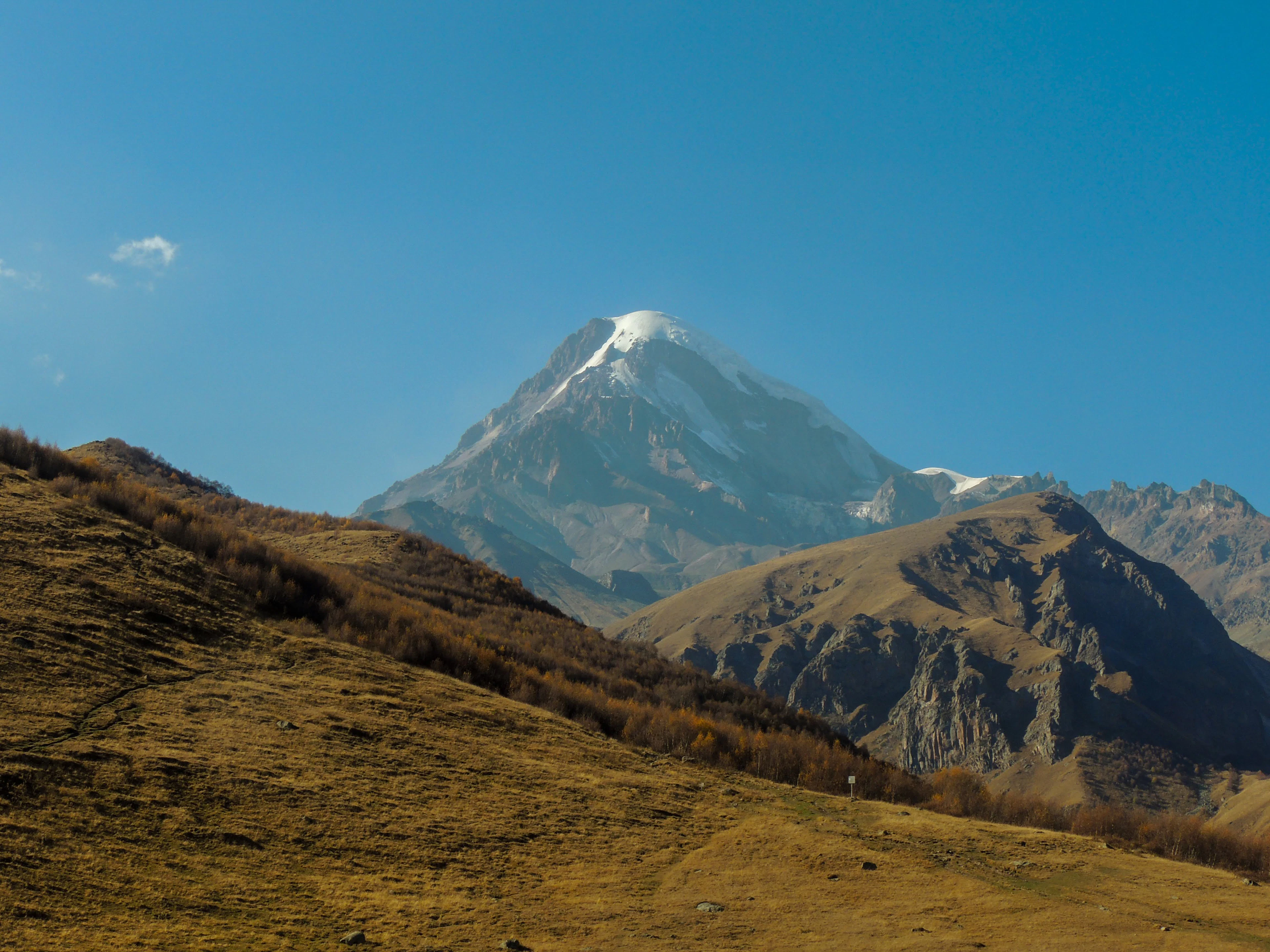 The snowy summit of Mount Kazbek above autumn-coloured slopes near Stepantsminda