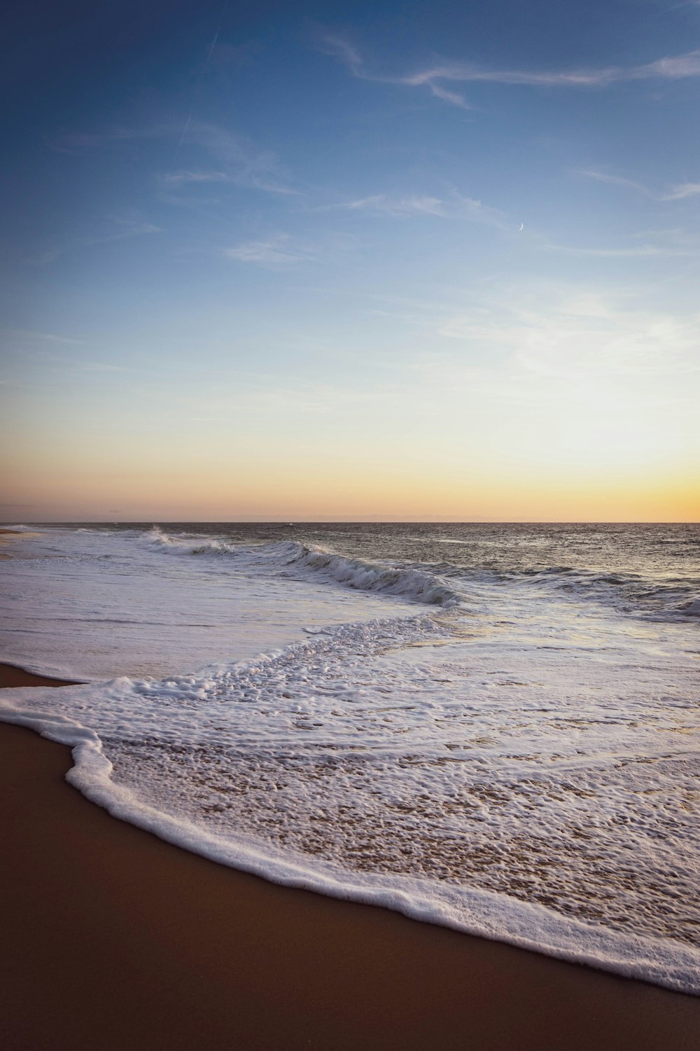 ocean waves crashing on shore during sunset