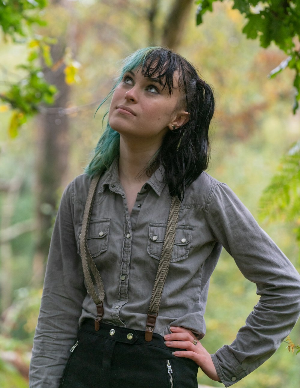 Femme en veste boutonnée en jean gris debout près d’arbres verts pendant la journée