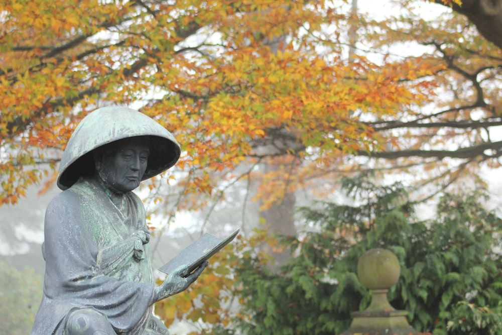 woman in gray hoodie and white hat standing near brown tree during daytime