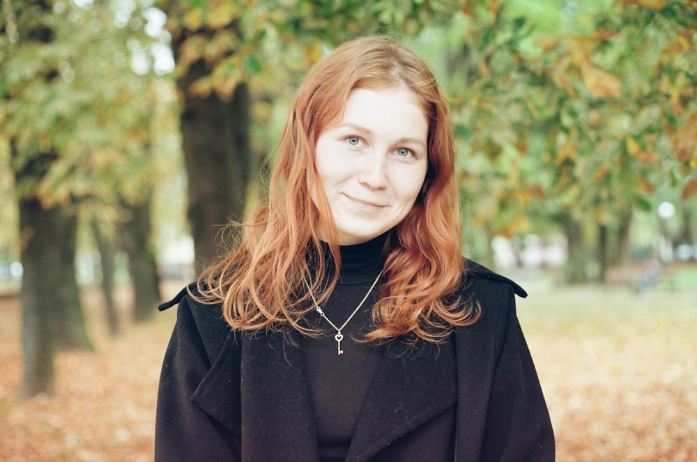 woman in black coat standing near green trees during daytime