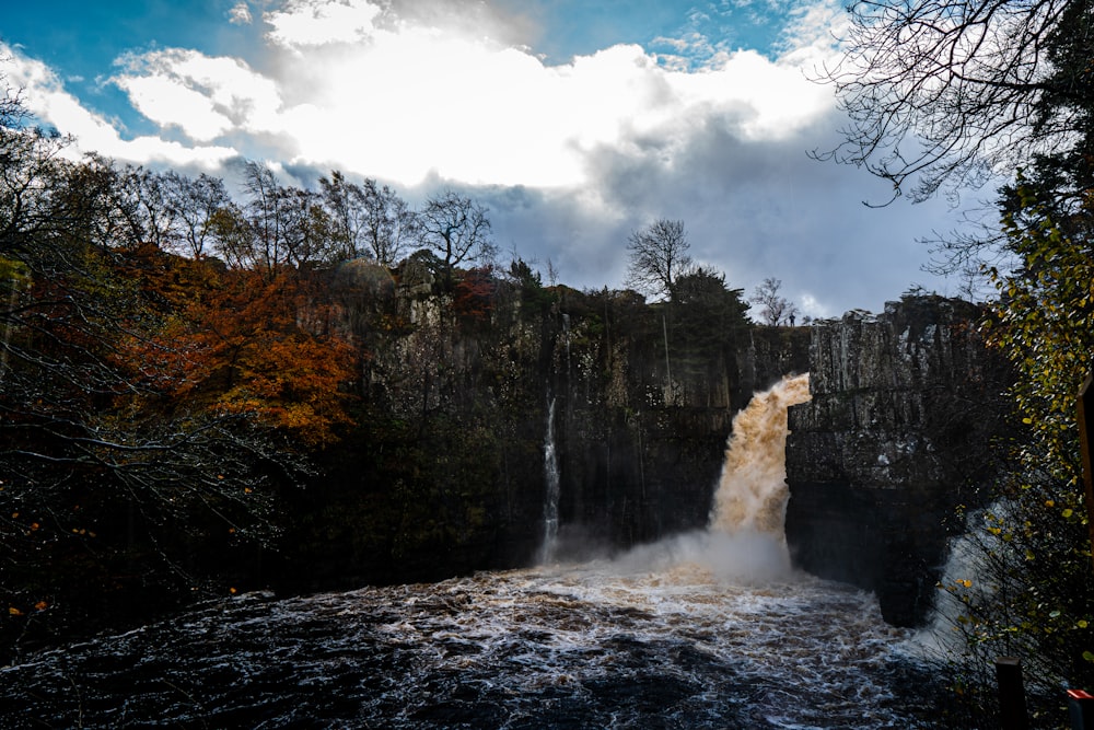 cascadas cerca de árboles verdes bajo nubes blancas durante el día