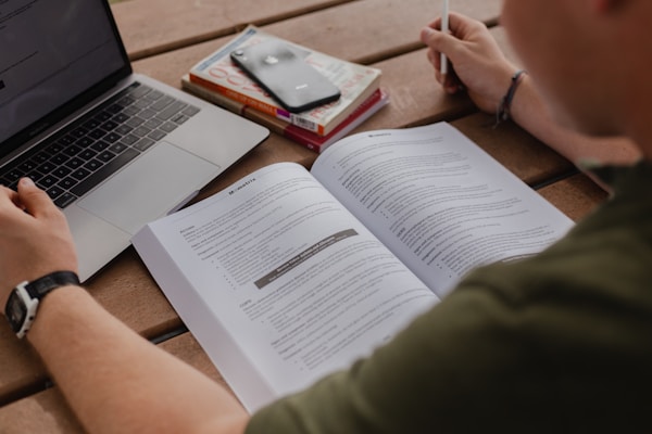 Medical student in white coat studying with books and laptop in modern library