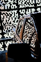 A shiny car is parked with an intricate pattern of small rectangular lights reflecting on its surface. The background features a decorative wall with geometric designs created by the same light pattern.