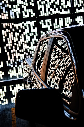 A shiny car is parked with an intricate pattern of small rectangular lights reflecting on its surface. The background features a decorative wall with geometric designs created by the same light pattern.