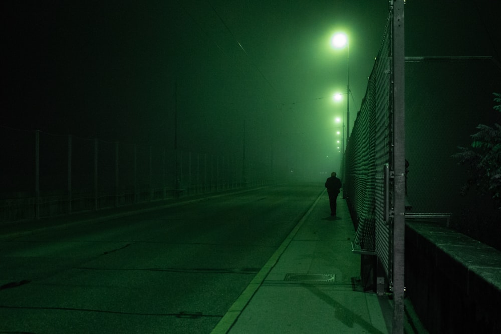 uomo in giacca nera che cammina sul marciapiede durante la notte