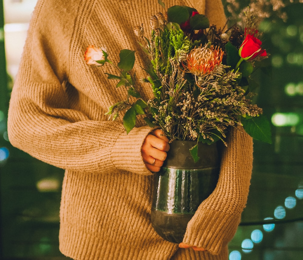 woman in brown sweater holding green and red flower bouquet