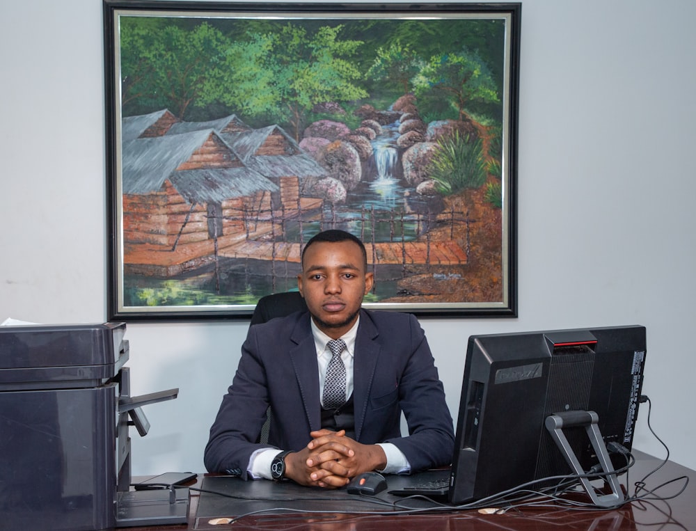 man in black suit jacket sitting on chair in front of black laptop computer