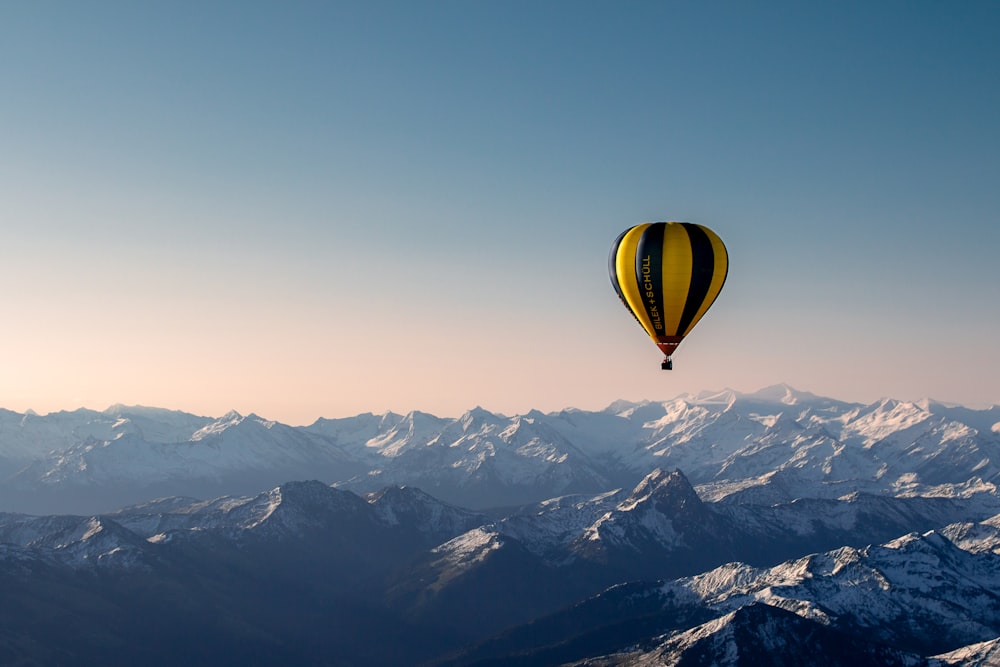 globo aerostático amarillo y azul que vuela sobre las montañas durante el día