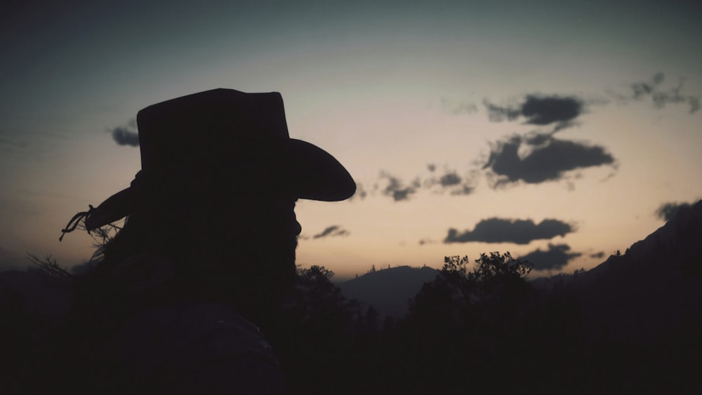 silhouette of person wearing cowboy hat during sunset
