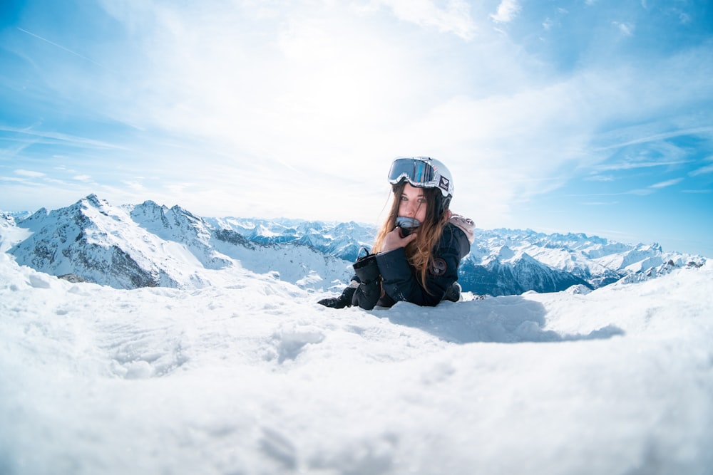 man in black jacket lying on snow covered ground