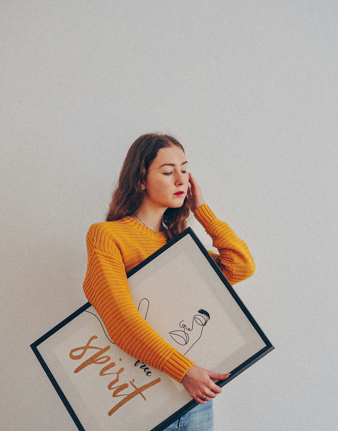 woman in yellow sweater holding black framed photo