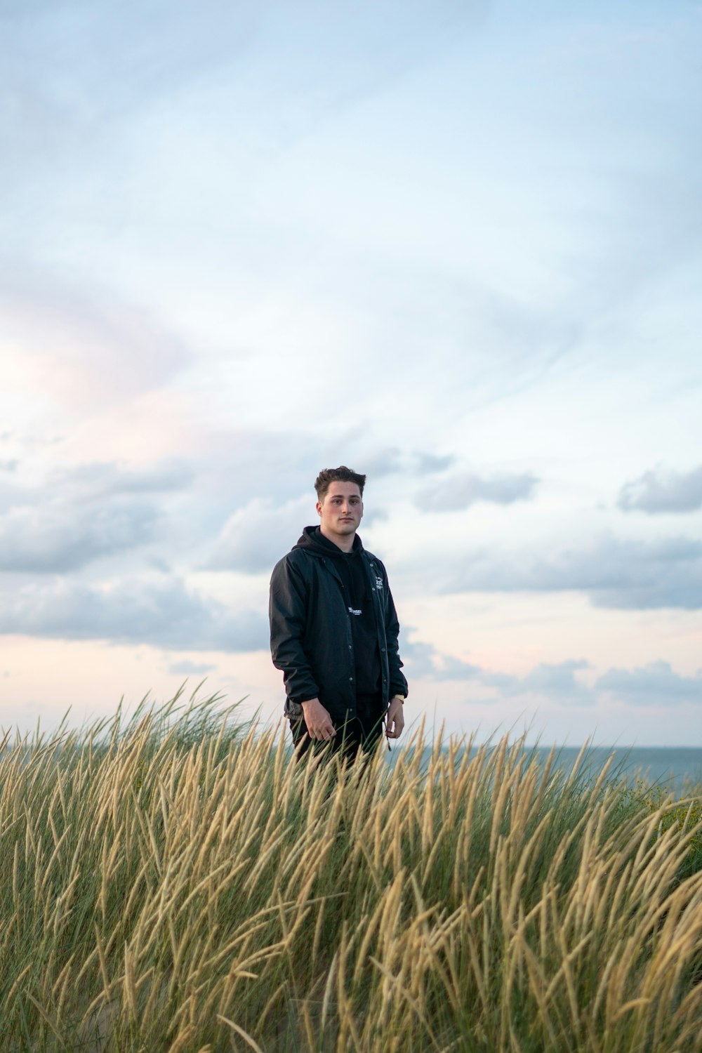 man in black jacket standing on green grass field under gray cloudy sky during daytime