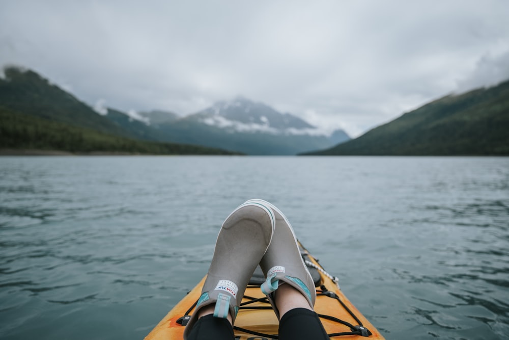 person in white shoes sitting on orange kayak on lake during daytime