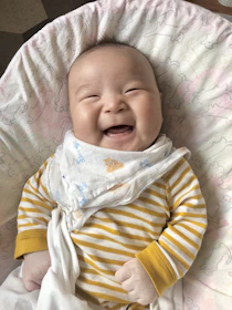 Smiling baby comfortably lying on a soft blanket wearing a Buckloo diaper.