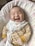 A smiling baby wearing cozy clothes sitting on a soft blanket.
